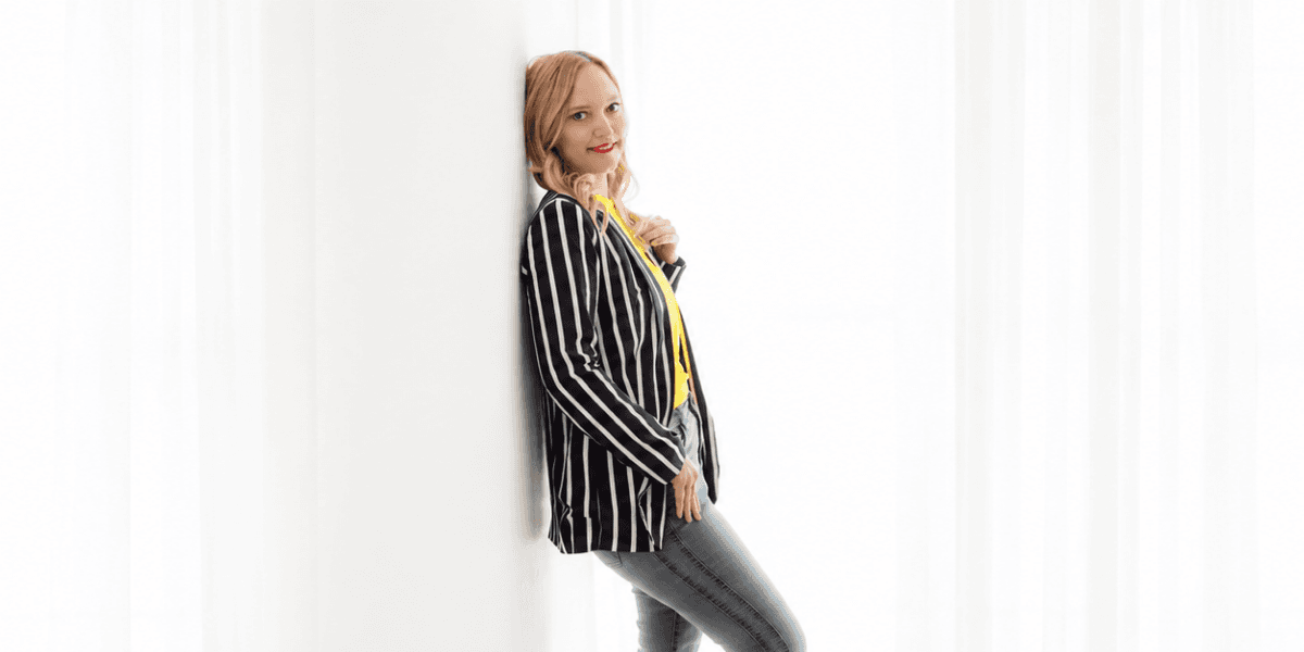 Woman in striped blazer and yellow top poses against a white backdrop