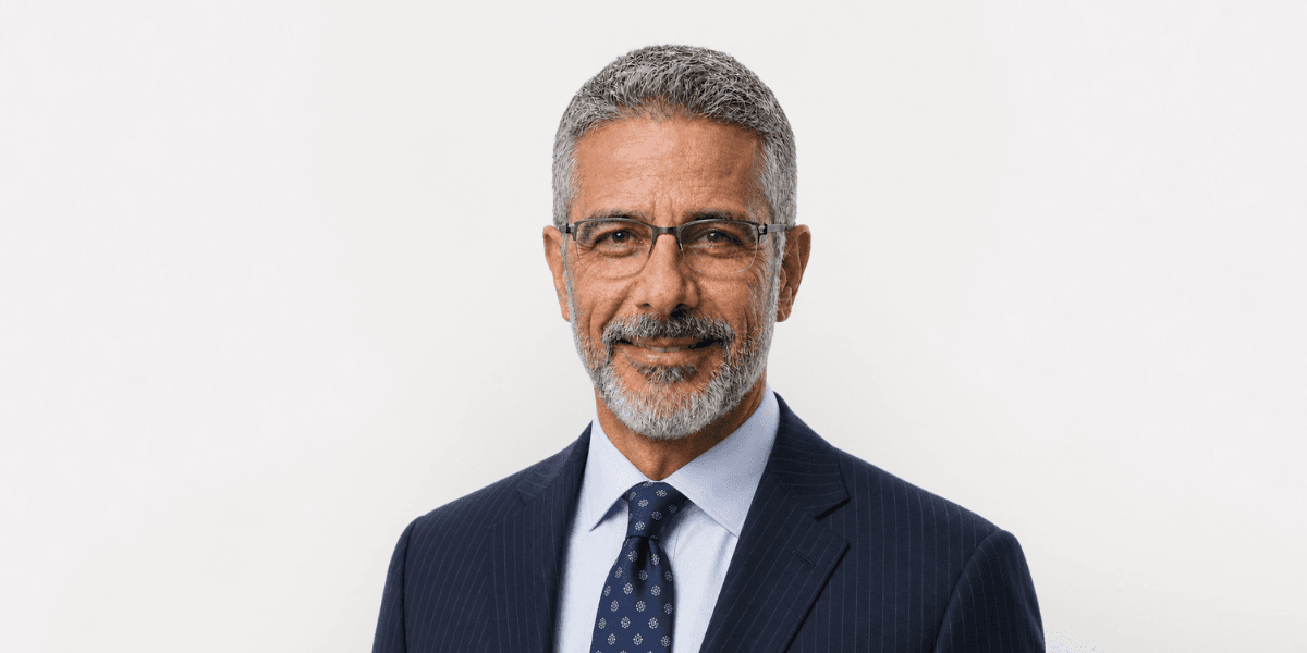 Smiling middle-aged man in glasses, wearing a navy suit and patterned tie.