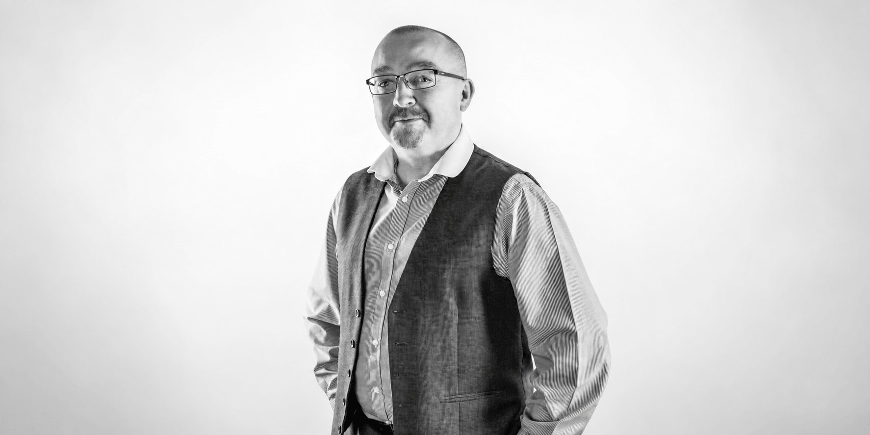A man in a vest and shirt poses confidently against a light backdrop