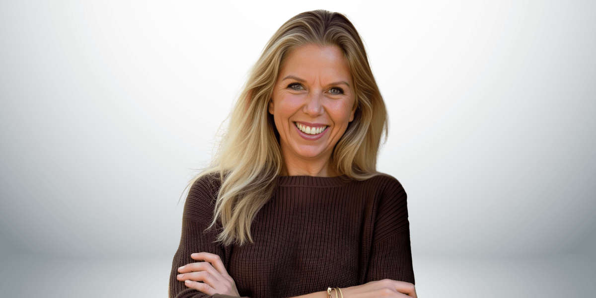 Smiling woman with long blonde hair wearing a brown sweater, arms crossed.
