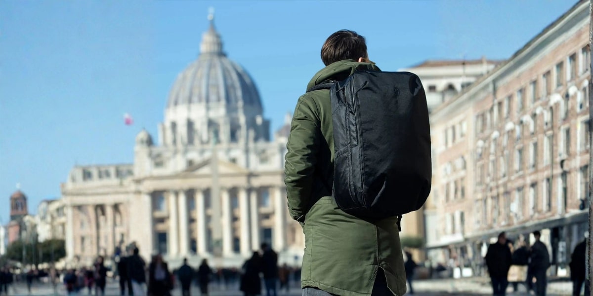 a man with a backpack in front of a historic building, evoking themes of travel, mentorship, and cultural exploration.