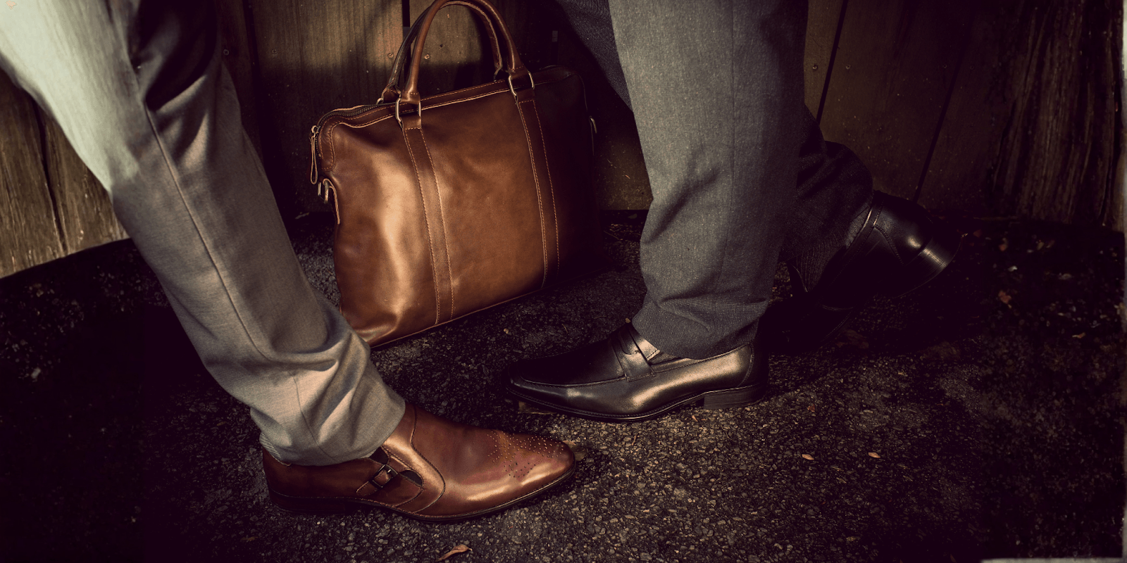 Two individuals wearing stylish leather shoes, one brown and one black, standing with a brown leather bag, symbolizing high-end corporate gifting.