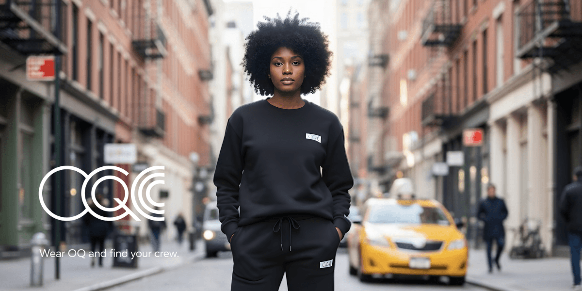 Model wearing minimalist black sweatshirt and joggers in city street, promoting "Wear OQ and find your crew."