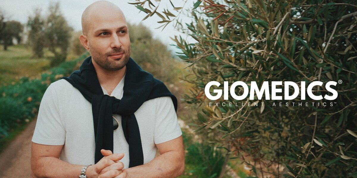 Physician founder outdoors beside olive trees with GIOMEDICS® branding, highlighting the company’s European aesthetic vision.