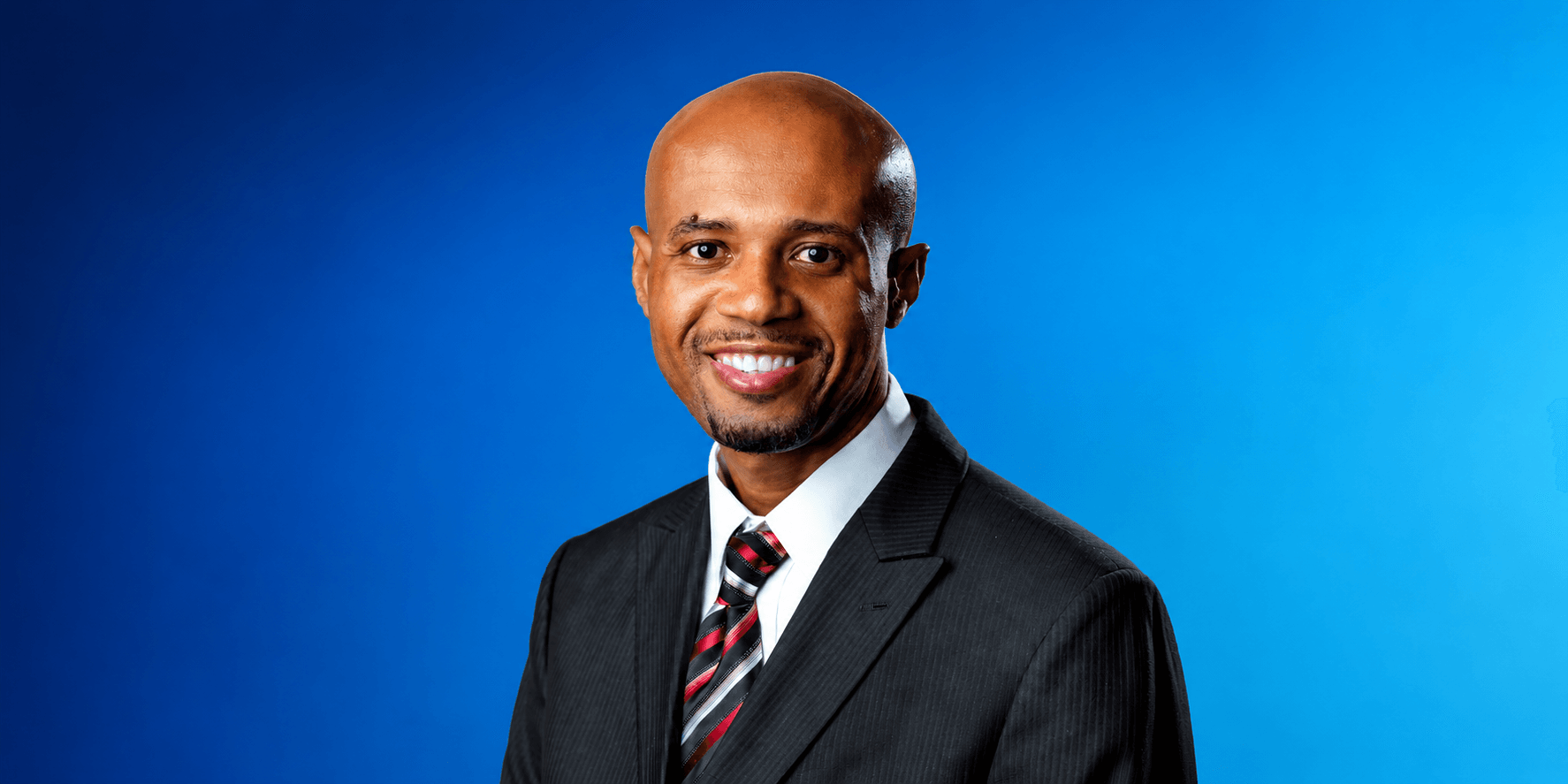 Professional portrait of Dr. Randrick Chance in a business suit against a blue background.