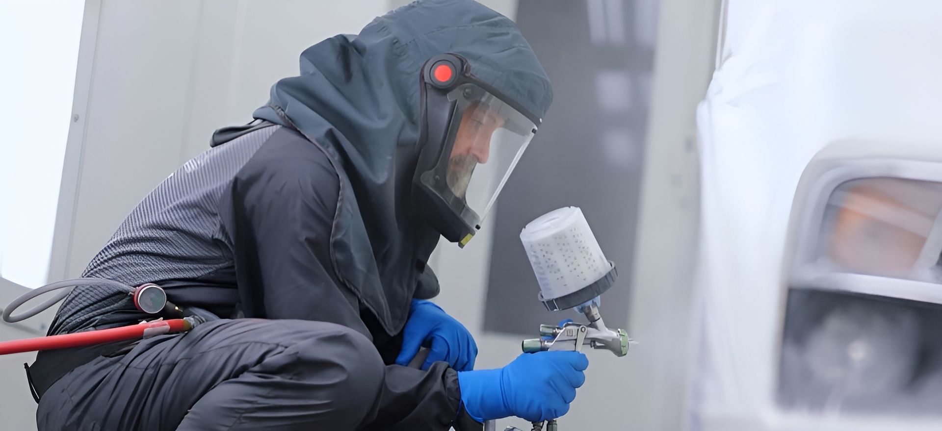 Worker in protective gear spray-painting a vehicle in a controlled environment.