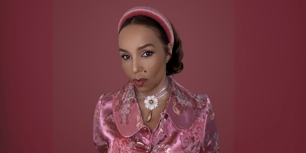 Woman in pink floral outfit and headband wearing a daisy pendant necklace.