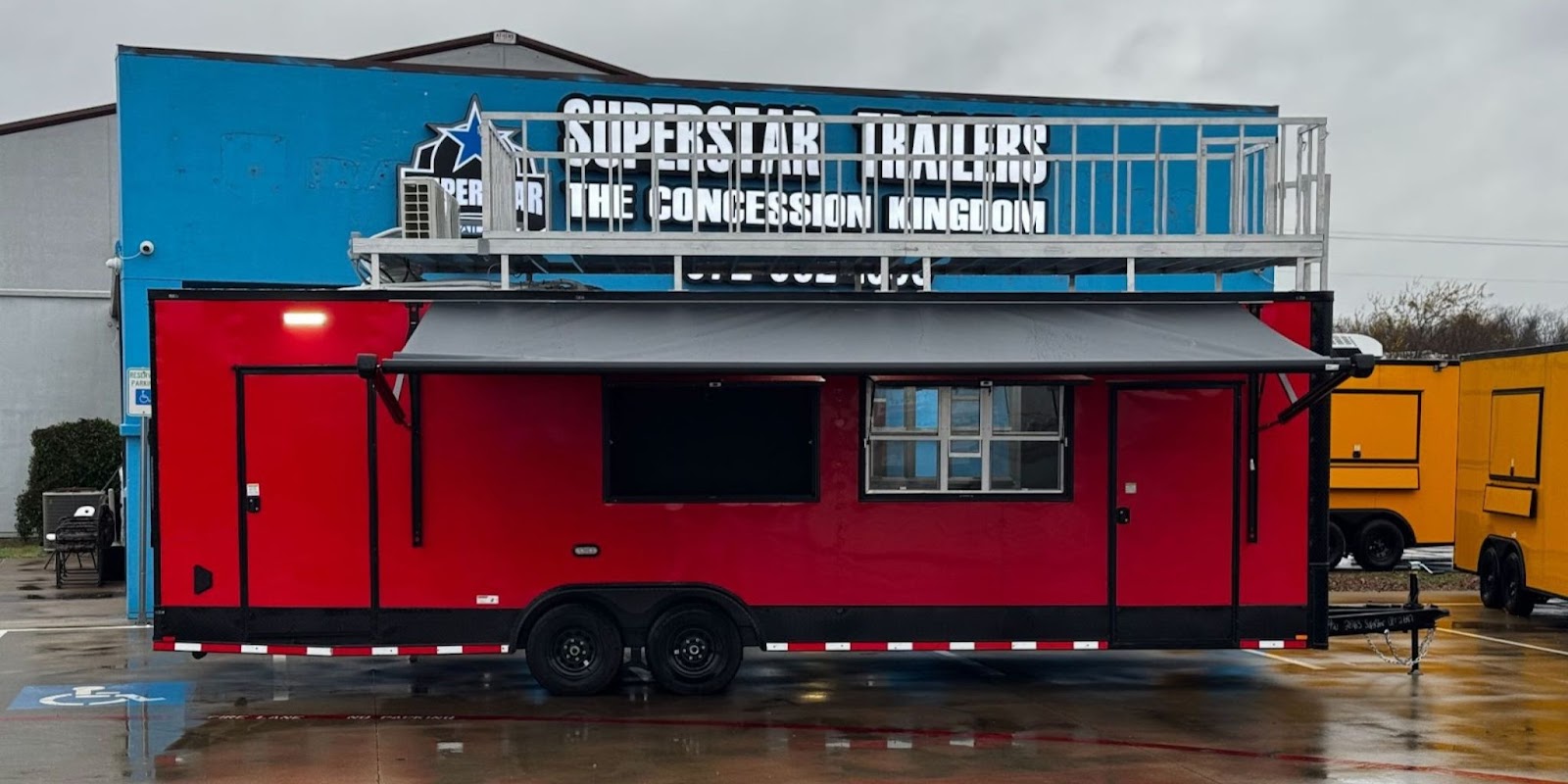 Red custom concession trailer with awning parked outside Superstar Trailers, a leading custom trailer dealership in Texas.