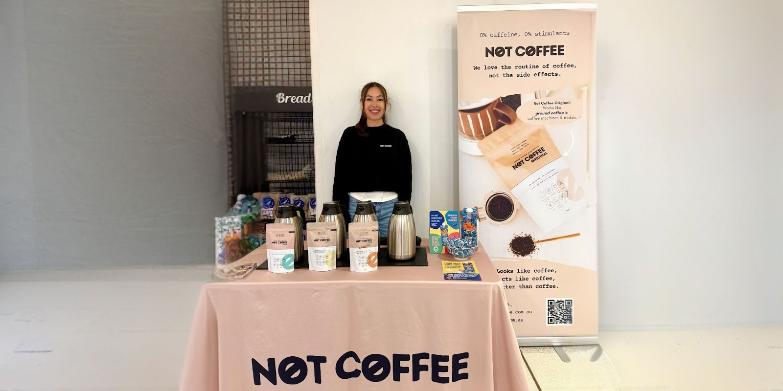 Smiling woman stands at Not Coffee booth promoting caffeine-free coffee alternatives with samples and branded materials.