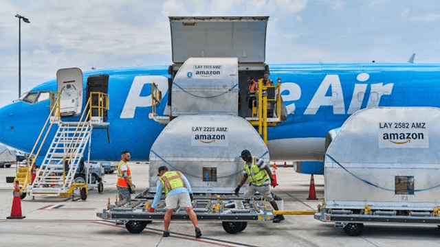 Workers load cargo containers onto a Prime Air aircraft at an airport.