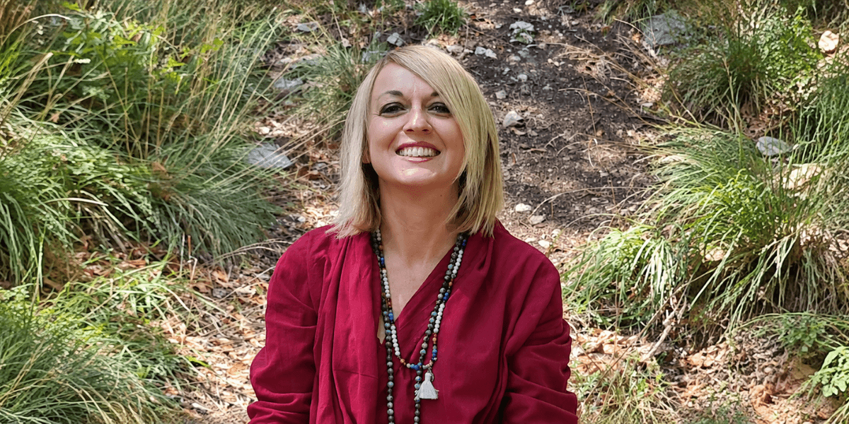 Smiling woman in a red outfit sitting in a natural, grassy outdoor setting