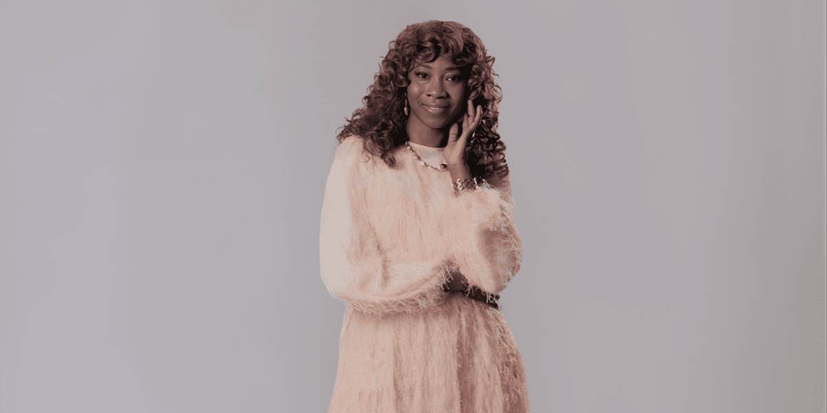 A woman with curly hair in a fluffy, light-colored dress poses elegantly against a neutral background