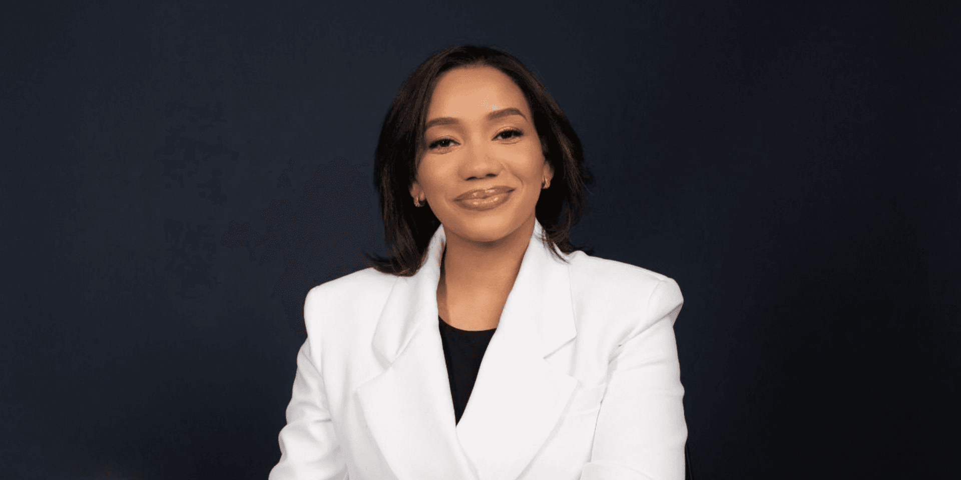 A professional woman in a white blazer smiles against a dark background