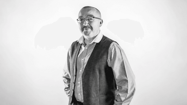 A man in a vest and shirt poses confidently against a light backdrop