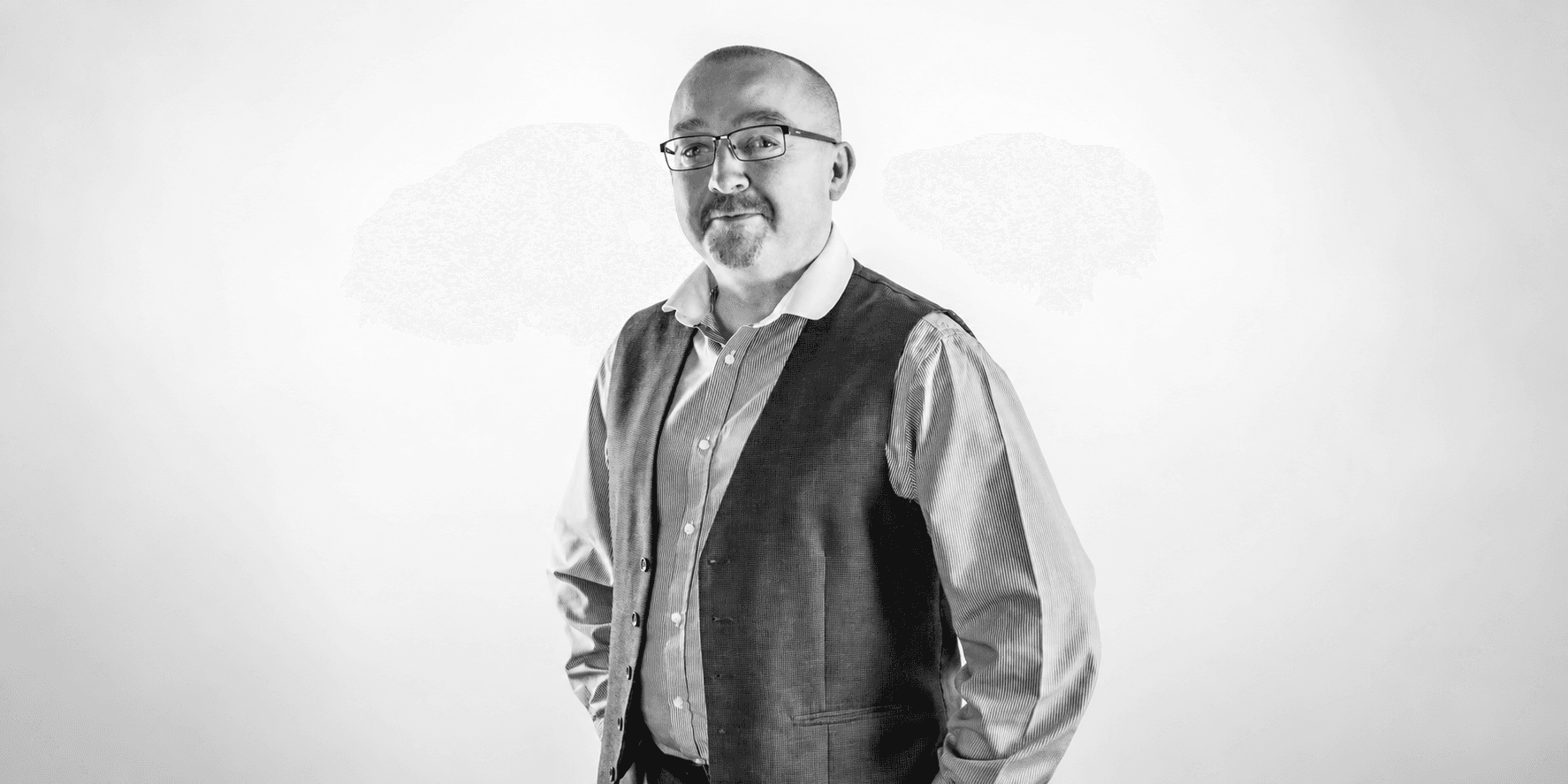 A man in a vest and shirt poses confidently against a light backdrop