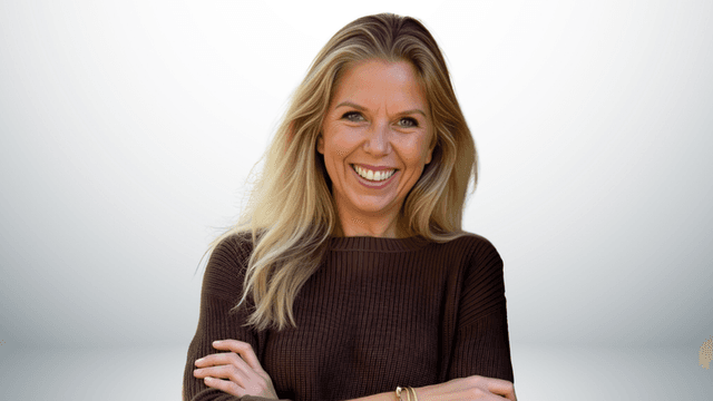 Smiling woman with long blonde hair wearing a brown sweater, arms crossed.