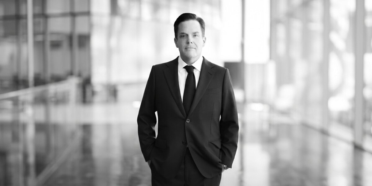 Paul Scribner wearing a dark suit and tie in a modern professional setting.