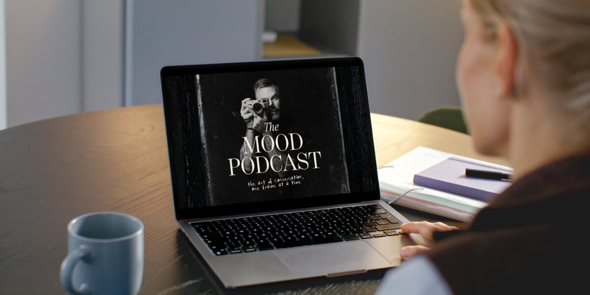 A woman sits at a table with a laptop and a book, engaged in thoughtful work or study, embodying a creative atmosphere.