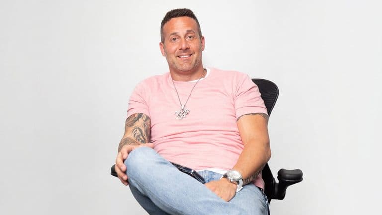 10X BNB Guy representative seated in an office chair wearing a pink shirt and jeans.