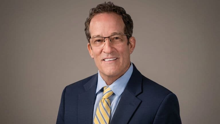 John Ziesing wearing a navy suit, blue shirt, and yellow striped tie.