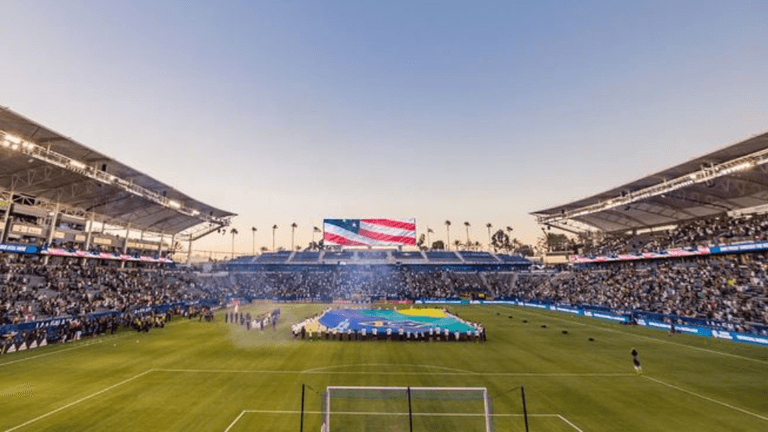 Crowded soccer stadium during a field ceremony with large flags displayed at center field.