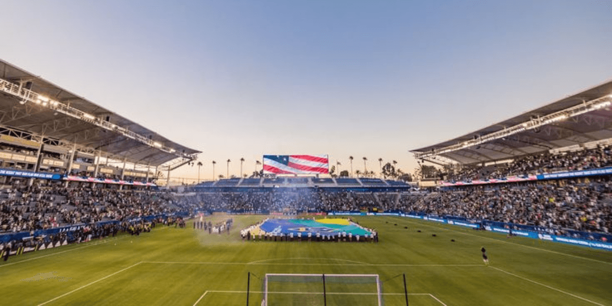 Crowded soccer stadium during a field ceremony with large flags displayed at center field.